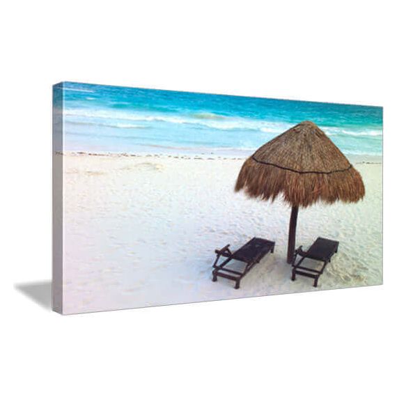 Beach scene with thatched umbrella and lounge chairs on white sand, turquoise ocean in the background.