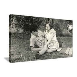 Black and white vintage photo of a man and girl sitting on grass, enjoying a playful moment together.